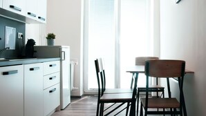 Moderni keittiö, jossa on valkoiset kaapit, ruokapöytä tuoleineen ja suuri ikkuna, jossa on sälekaihtimet.