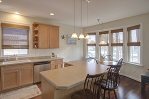 A kitchen with wooden cabinets, a dishwasher, a large island with chairs, pendant lights, and large windows with blinds. - Sweet Water View/Access 2 BR 10 Minutes to Bethany Beach w/Kayaks and Activities Sleeping 4 (Ocean View)