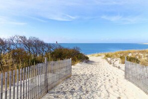 A sandy beach path leading to the ocean with a lighthouse in the distance. - Pet Friendly Water Front Cottage Sleeping 8 with Kayaks and More Free Activities (Ocean View)