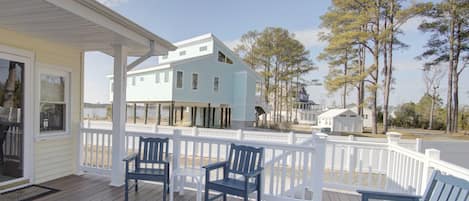Une terrasse en bois avec une balustrade blanche, trois fauteuils Adirondack bleu foncé et une maison bleu clair avec un porche blanc.