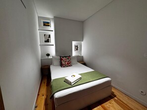 A small, modern bedroom with a single bed, a green throw blanket, and a small bedside table with a plant. - Stylish Lisbon Stay, Renovated Gem in Bairro Alto with A/C and one Bedroom (Lisboa)