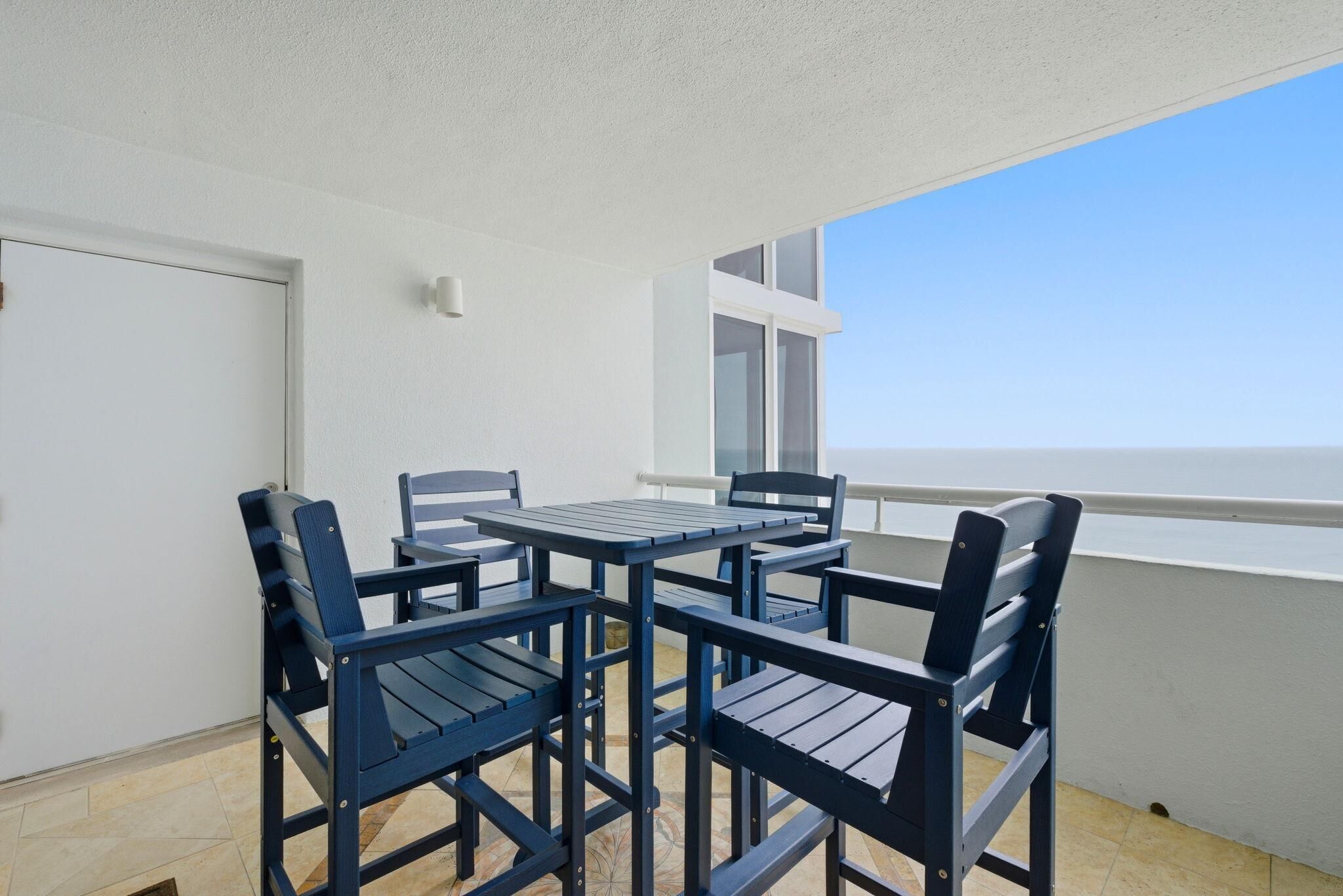 Un balcon avec une table et des chaises, une porte blanche et une vue sur la mer.
