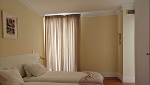 Ein Hotelzimmer mit zwei Betten, einem großen Fenster mit Vorhängen, einem Bild an der Wand und einem Kleiderschrank.
