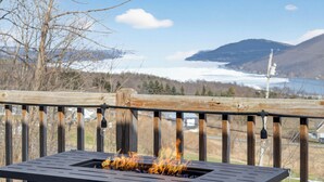 Une terrasse dotée d’un foyer extérieur, offrant une vue panoramique sur un paysage magnifique, avec des montagnes et une étendue d’eau.