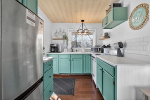 Una cocina con gabinetes color turquesa, un refrigerador de acero inoxidable, un microondas y una cafetera.