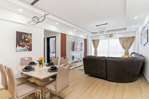 En moderne stue med sofa, spiseplads med borddækning, og et fjernsyn ophængt på væggen.