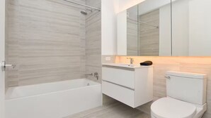 A modern bathroom with a bathtub, a toilet, and a vanity with a mirror. - Suites at Dog Lane (Mansfield)