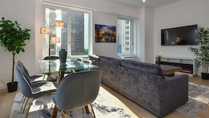 A modern living room with a glass dining table, grey sofa, and a flat-screen TV mounted on the wall. - Suites at Dog Lane (Mansfield)
