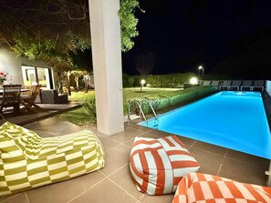 Un espace extérieur avec une piscine, une terrasse carrelée, un escalier pour accéder à la piscine et deux fauteuils en forme de sac.