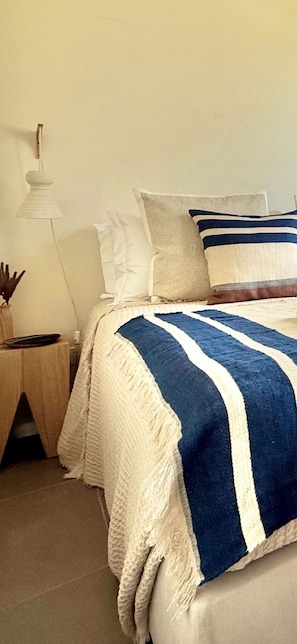 Un lit avec une couverture à rayures bleues et blanches, un oreiller blanc et un oreiller beige.