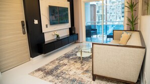 A modern living room with a sofa, a glass coffee table, a mounted TV, and a balcony with outdoor furniture. - Fabulous apartment in the center of jarabacoa rep dom. (Jarabacoa)