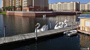 A waterfront hotel with multiple buildings, a dock with swans, and a small boat. - Westgate Town Center! Cozy 1-bdrm resort in tranquil Kissimmee with mult pools (Kissimmee)