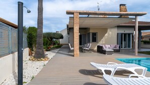 A modern outdoor patio with a pool, lounge chairs, and a covered seating area.