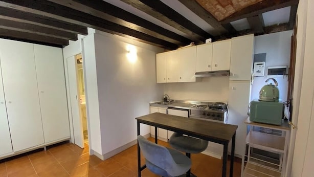 A compact kitchen with white cabinets, a gas stove, and a small table with two stools. - Luky lovely place in the very heart of central Venice (Venezia)