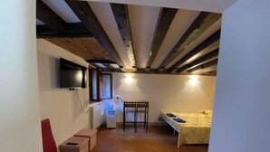 A compact room with a bed, a small table, a chair, a radiator, and a television mounted on the wall. - Luky lovely place in the very heart of central Venice (Venezia)