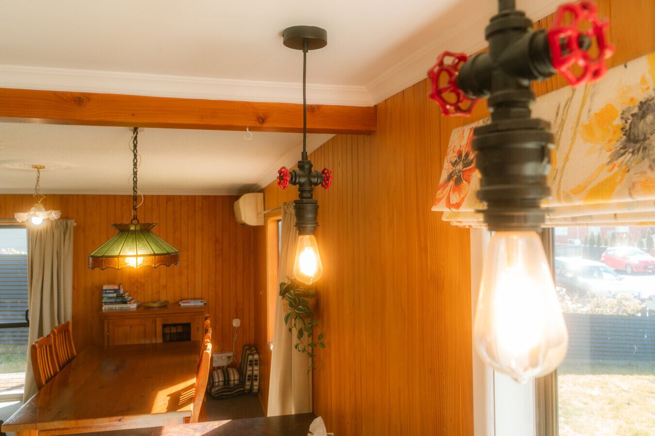 A cozy room with wooden walls, a dining table, and hanging lamps.
