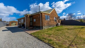 A single-story wooden house with a sloped roof, a front garage, and a gravel driveway. - Timber & Stars Cabin - your cosy getaway in the heart of Twizel. (Twizel)