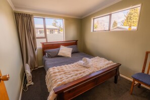 Ein Schlafzimmer mit einem hölzernen Bett, einem Sessel, einem Fenster und einem Ventilator.