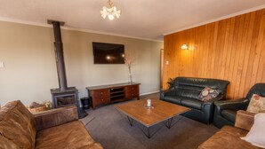 A living room with a fireplace, leather sofas, a coffee table, and a wooden wall panel. - Timber & Stars Cabin - your cosy getaway in the heart of Twizel. (Twizel)