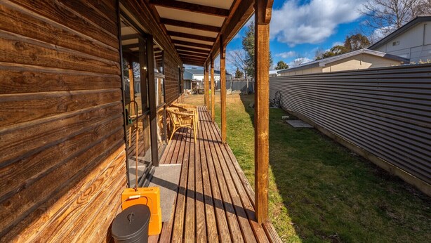 A wooden deck with a covered patio area, outdoor furniture, and a metal fence in the background. - Timber & Stars Cabin - your cosy getaway in the heart of Twizel. (Twizel)