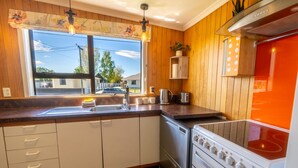 A kitchen with wooden paneling, a stainless steel stove, a sink, and a window with a view of houses outside. - Timber & Stars Cabin - your cosy getaway in the heart of Twizel. (Twizel)