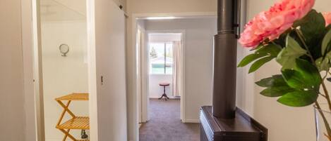 A hallway with a black wood-burning stove, a wooden shelf unit, and a pink flower in a vase.
