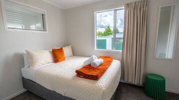 A hotel room with a bed, a window with curtains, a green stool, and a mirror on the wall.