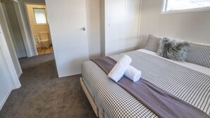 Ett hotellrum med en säng, ett fönster, en dörr och ett badrum som syns genom en öppen dörr.