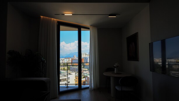 A modern hotel room with a large sliding glass door leading to a balcony with a city view. - One Bedroom Apartment with City and Mountain View (Tiranë)