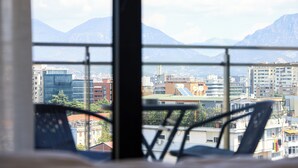 A view from a window with a metal railing, overlooking a cityscape with buildings and mountains in the background. - One Bedroom Apartment with City and Mountain View (Tiranë)