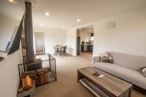A living room with a sofa, coffee table, and a fireplace. There is a dining area with a table and chairs in the background. - Hallewell Hideaway - Twizel (Twizel)