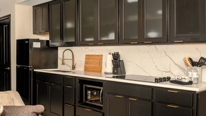 A modern kitchen with dark cabinetry, a stainless steel refrigerator, a built-in oven, and a marble backsplash.