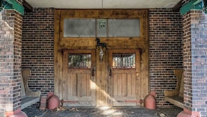 A wooden double door with a glass panel, flanked by brick walls and a bench.