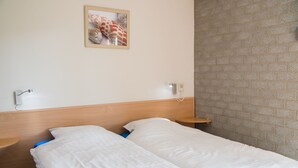 Ein Doppelbett mit weißen Leinen, ein Holz-Kopfbrett, ein kleiner Nachttisch und ein an der Wand befestigtes Telefon.