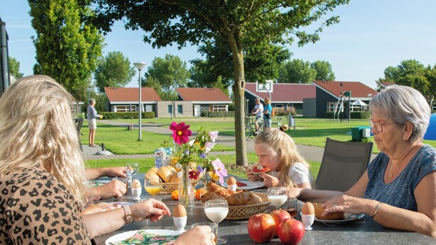 Eine Gruppe von Personen speist draußen an einem Tisch mit Essen und Getränken.