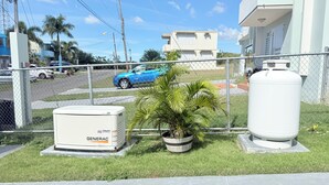 A fenced outdoor area with a Generac generator, a potted palm tree, and a large white tank. - Sun Beach Escape – Vacation Rental in Boquerón, Cabo Rojo (Boquerón)