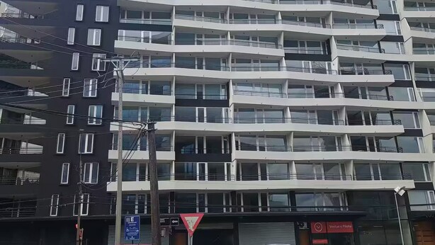Ein mehrstöckiges Gebäude mit Balkonen, ein rotes Auto und ein weißes Auto vor der Fassade.
