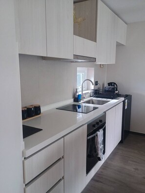 A modern kitchen with white cabinetry, a black stovetop, and a stainless steel sink. - Modern apartment in the heart of Puerto Montt (Puerto Montt)