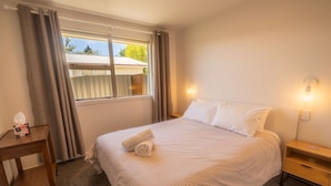 Une chambre d’hôtel comprenant un lit, une table de chevet, une commode, une fenêtre avec des rideaux et une vue sur l’extérieur.