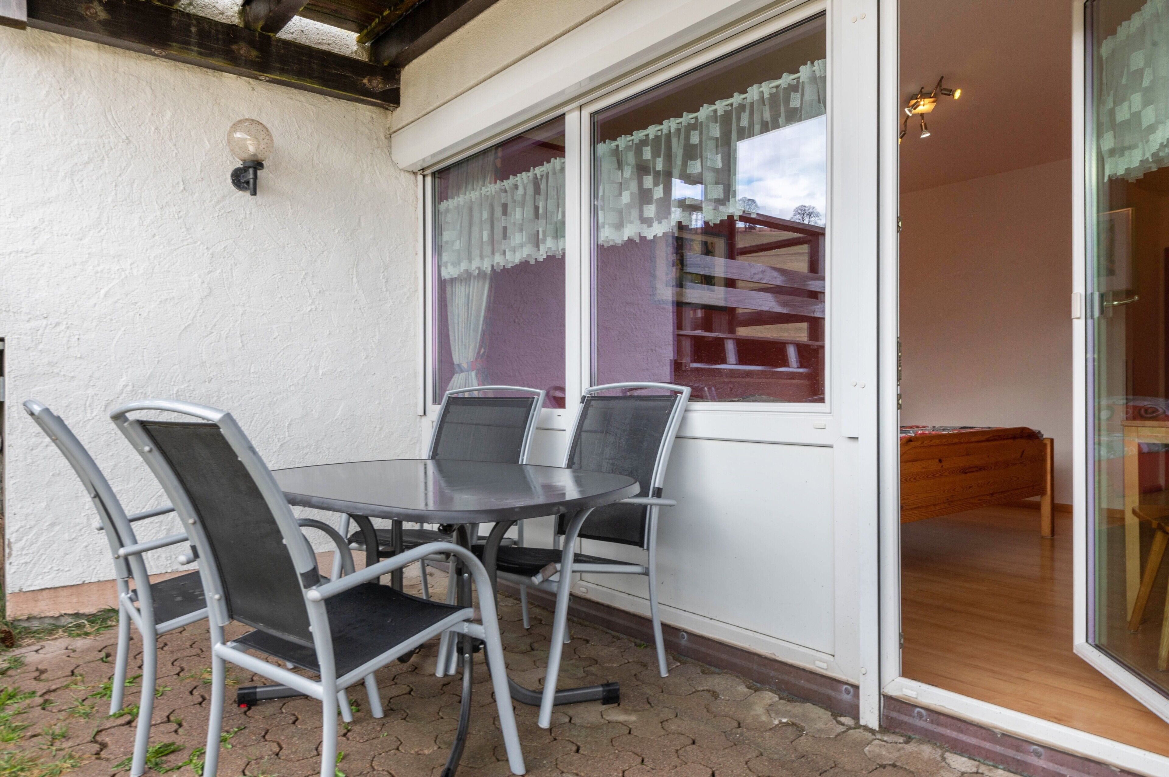 A patio with a table and chairs, a sliding glass door, and a wooden bench inside.