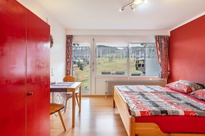 A bedroom with a large window, a bed with patterned bedding, a wooden chair, and a red wardrobe. - Apartment 'Fichte' with Mountain View, Shared Terrace and Wi-Fi (Todtnau)