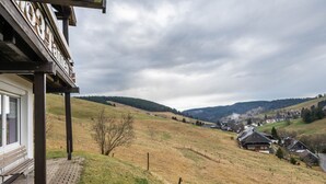 A rural landscape with a building featuring a porch and a bench, surrounded by rolling hills and a cloudy sky.