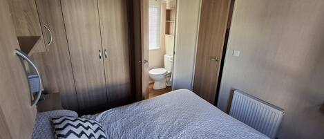 A bedroom with a bed, a wardrobe, a radiator, and a bathroom visible through an open door.