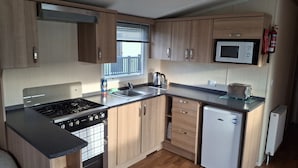 A compact kitchen with a stove, sink, microwave, and a small refrigerator. - Glasyln 37 (Porthmadog)