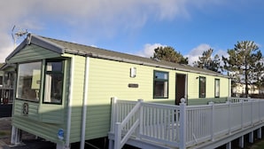 A single-story mobile home with a green exterior, a white porch, and a small deck area. - Glasyln 37 (Porthmadog)