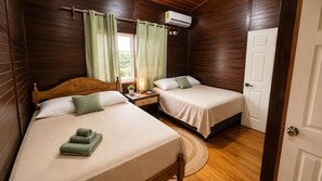 Una habitación con dos camas, una mesita de noche con lámpara, una ventana con cortinas y un equipo de aire acondicionado.