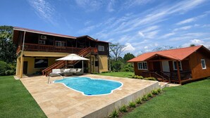 Una casa de dos pisos con piscina, mobiliario de exterior y un porche cubierto.