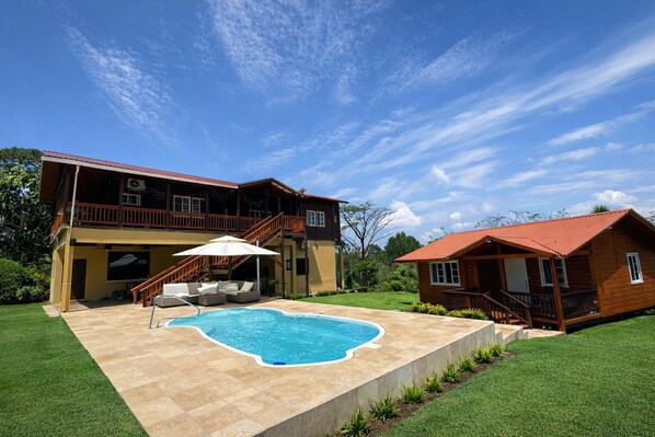 Ein zweistöckiges Haus mit Swimmingpool, Gartenmöbeln und einer überdachten Terrasse.