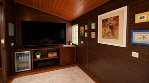 Habitación con televisor de pantalla plana grande, armarios de madera, refrigerador y cuadros en las paredes.
