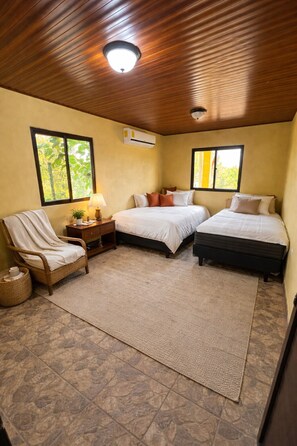 Una habitación con dos camas, una silla, una mesita de noche y un ventanal.